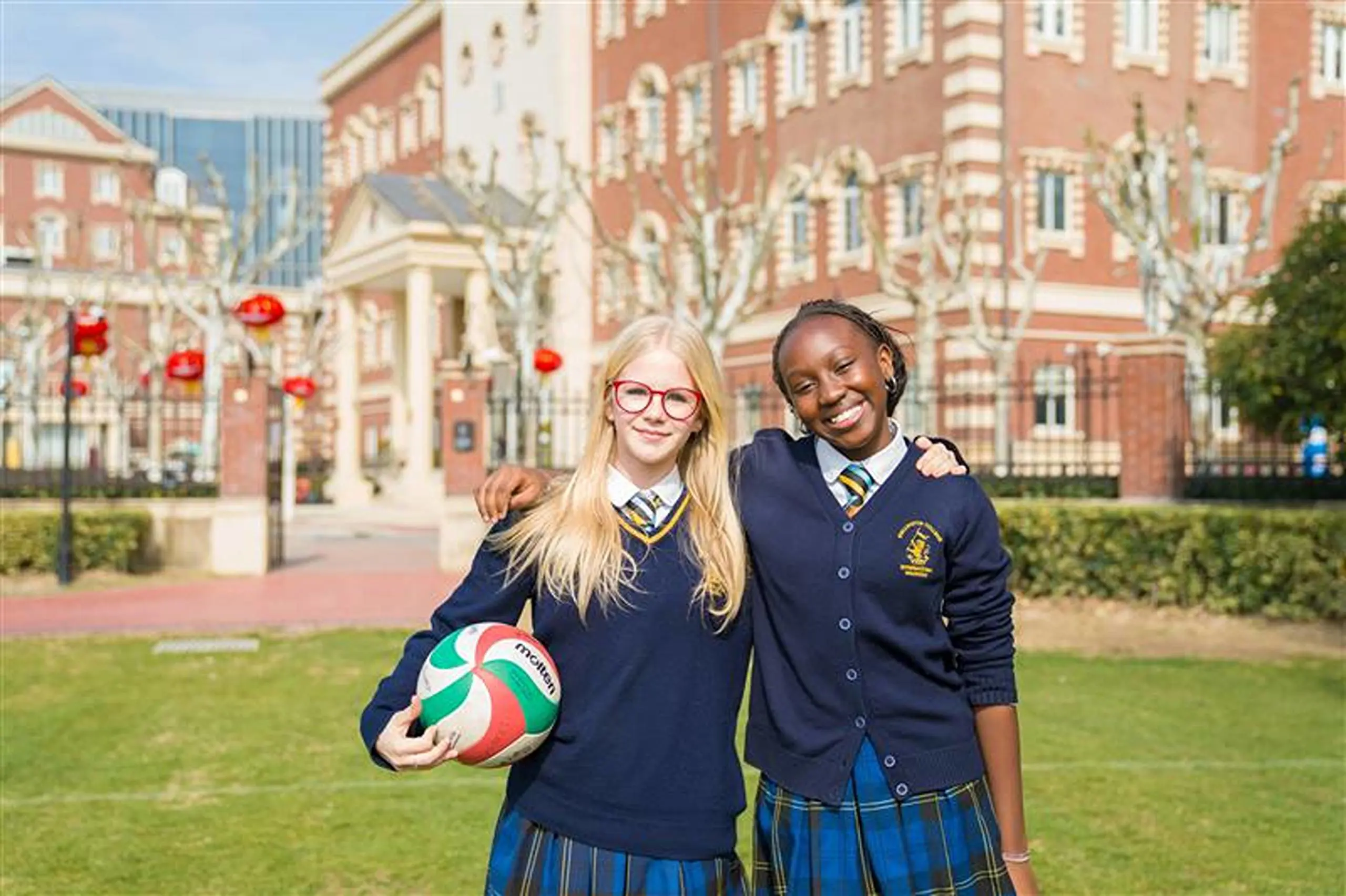 Students holding football and smiling in front of campus
