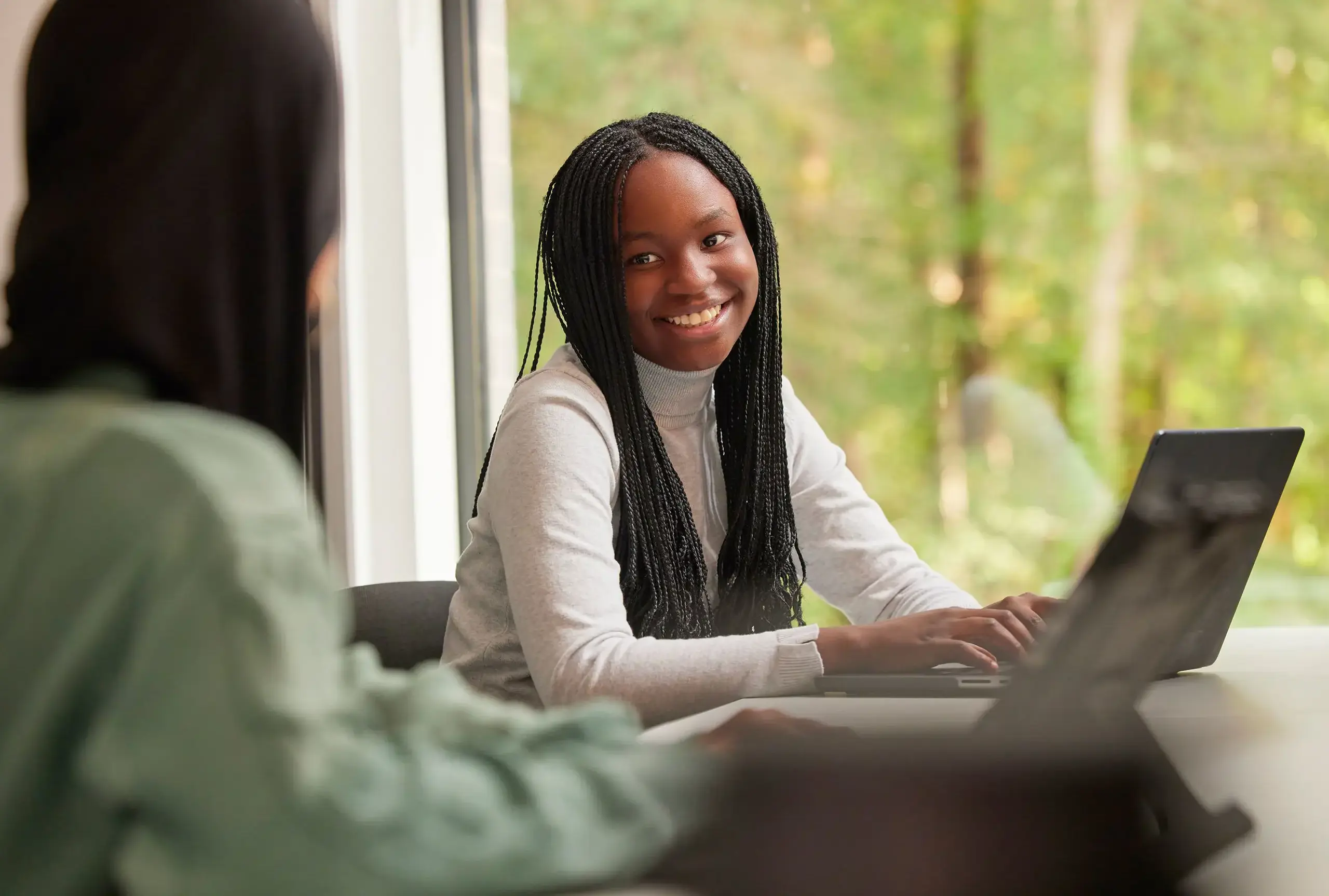 two girls smiling in Wellington Collegr dorms while working on laptops